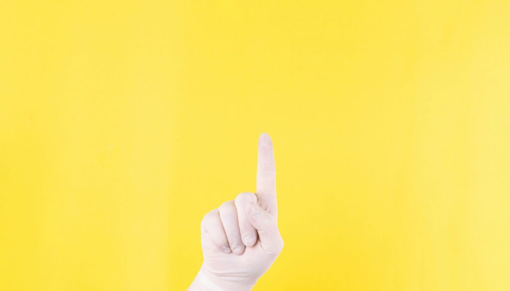 A hand holding up pointer finger on a yellow background. 