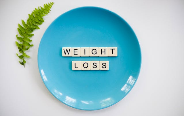 Caption: It's important to maintain a stable weight after surgery; however, you should avoid rapid weight loss methods and fad diets. Alt text: Blue plate and words Weight Loss in Scrabble letters on it, green leaf next to it.